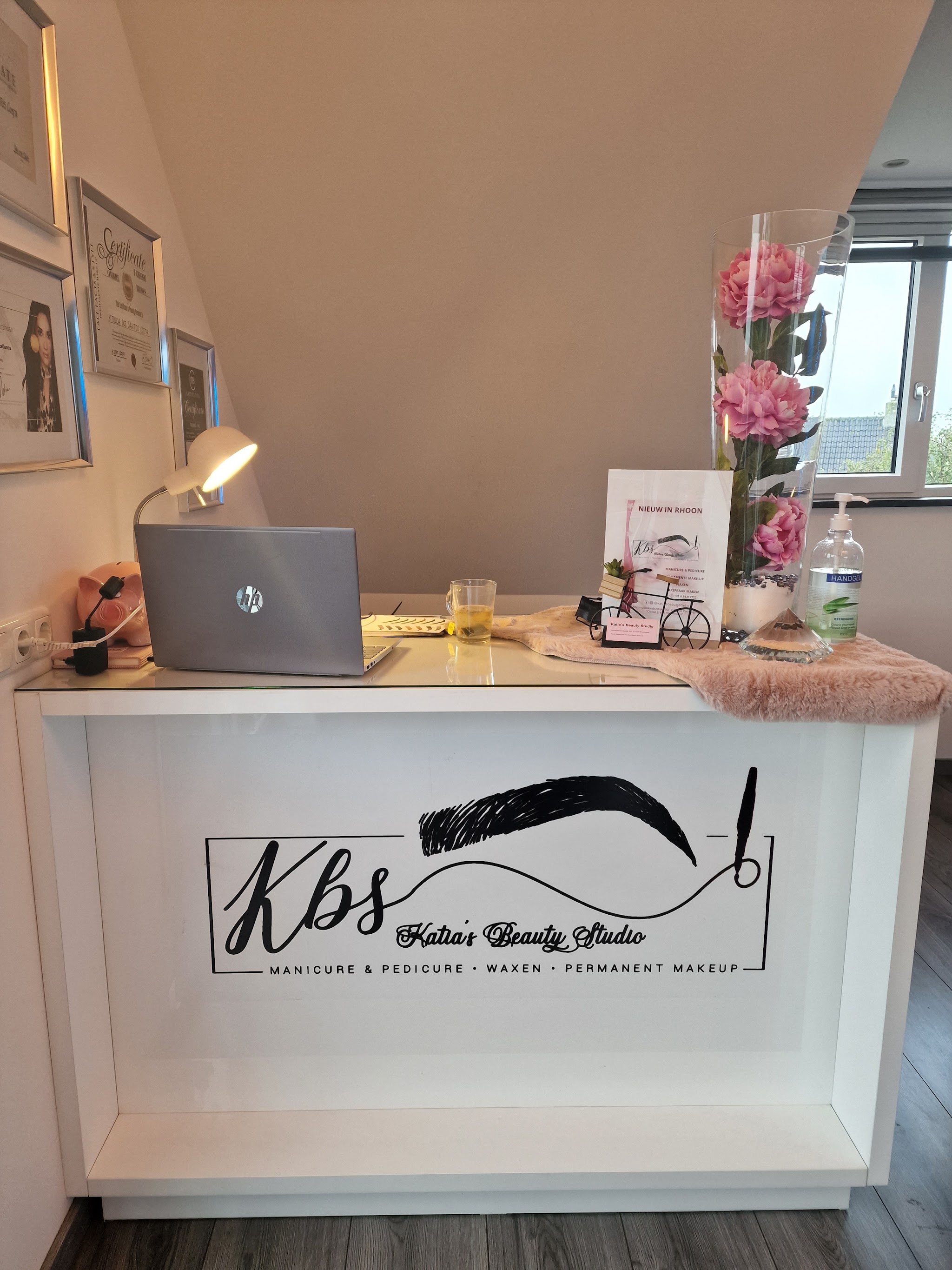 De balie van Katia's Beauty Studio met het logo, bloemen en een laptop